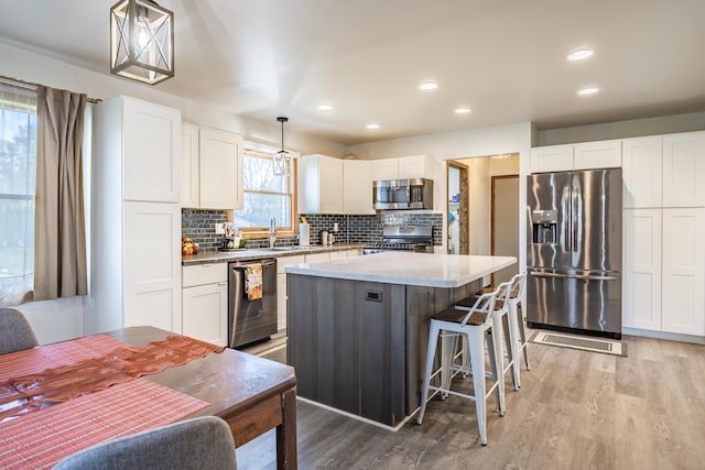 kitchen featuring light wood-type flooring, stainless steel appliances, a kitchen island, decorative light fixtures, and white cabinetry