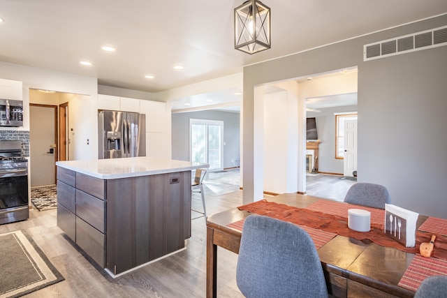 kitchen featuring white cabinetry, appliances with stainless steel finishes, pendant lighting, a kitchen island, and light wood-type flooring