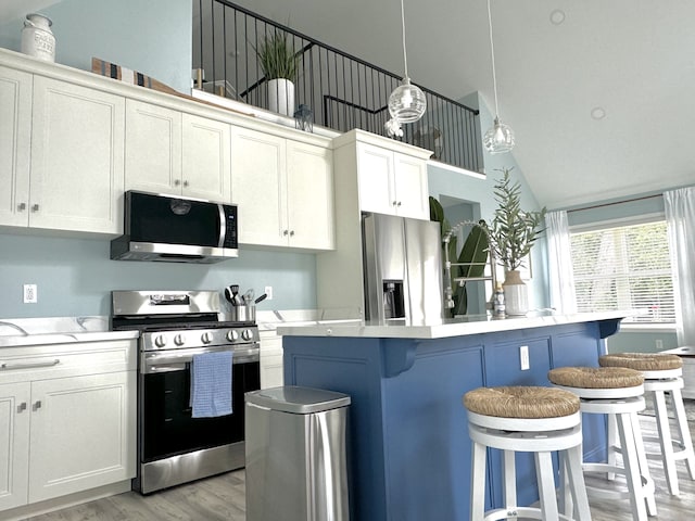 kitchen with a center island, decorative light fixtures, a kitchen bar, white cabinetry, and stainless steel appliances