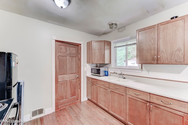 kitchen with light brown cabinetry, light wood-type flooring, black fridge, and sink