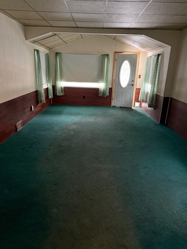 entryway featuring carpet flooring, wooden walls, and lofted ceiling