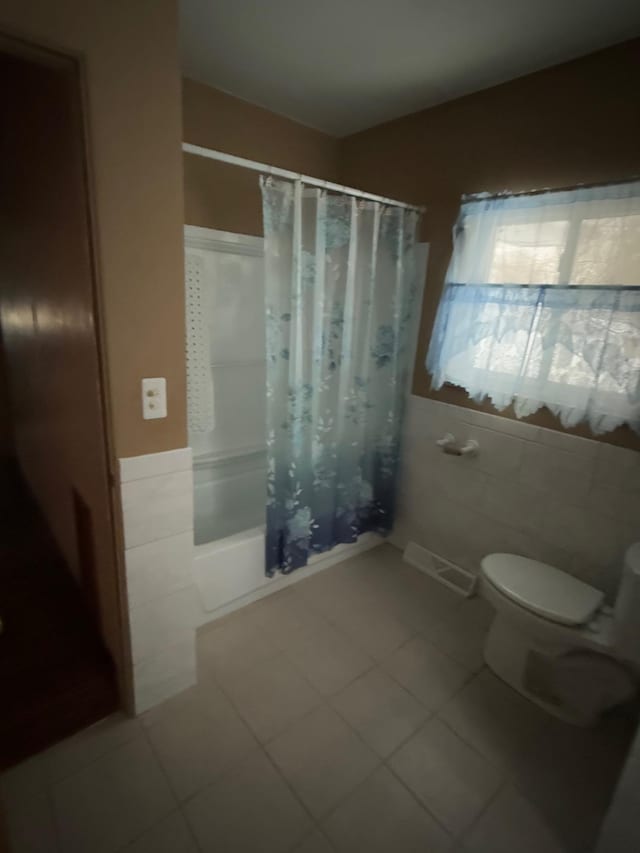 bathroom with tile patterned floors, toilet, shower / bathtub combination with curtain, and tile walls