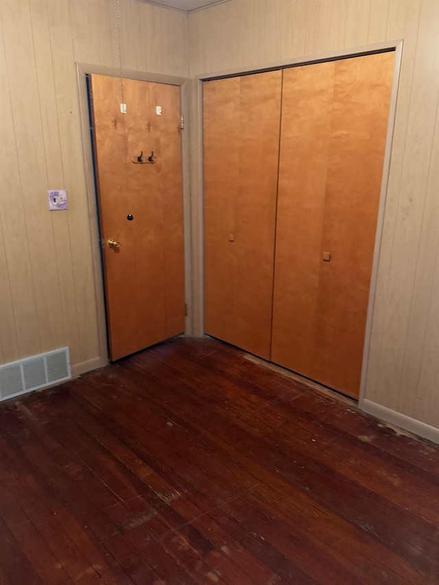 unfurnished bedroom featuring dark hardwood / wood-style floors, a closet, and wood walls