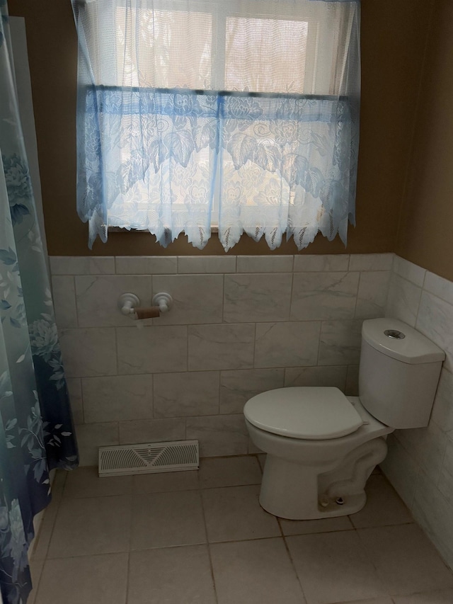 bathroom with tile patterned flooring, a healthy amount of sunlight, tile walls, and toilet