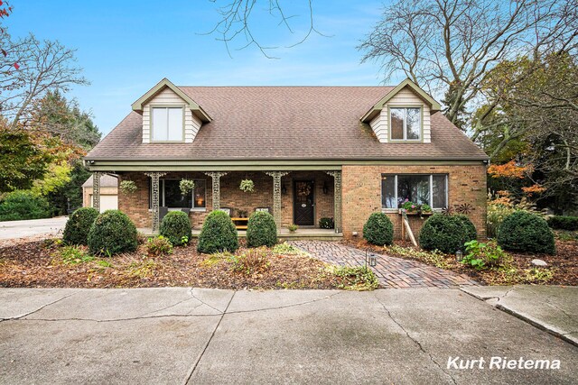 3205 Lakeshore Dr, Saint Joseph, MI 49085 - new england style home featuring covered porch, brick siding, a shingled roof, and a garage
