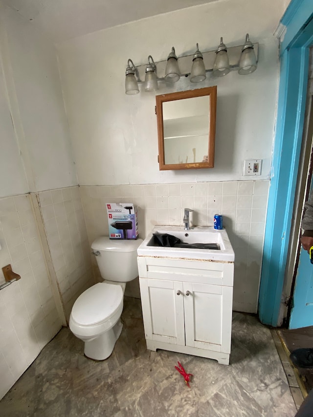 half bath with toilet, a wainscoted wall, tile walls, and vanity