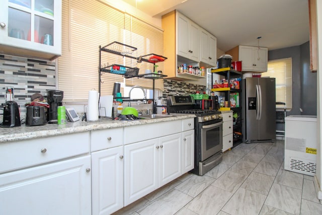 kitchen featuring appliances with stainless steel finishes, tasteful backsplash, light stone counters, sink, and white cabinetry