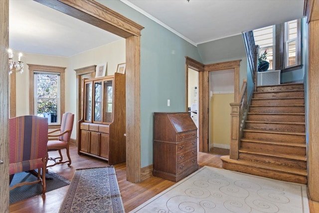 entryway with light hardwood / wood-style flooring, ornamental molding, and an inviting chandelier