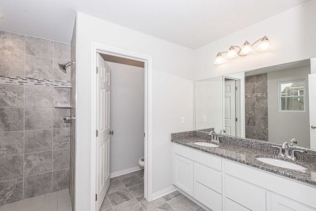 bathroom with a tile shower, vanity, and toilet