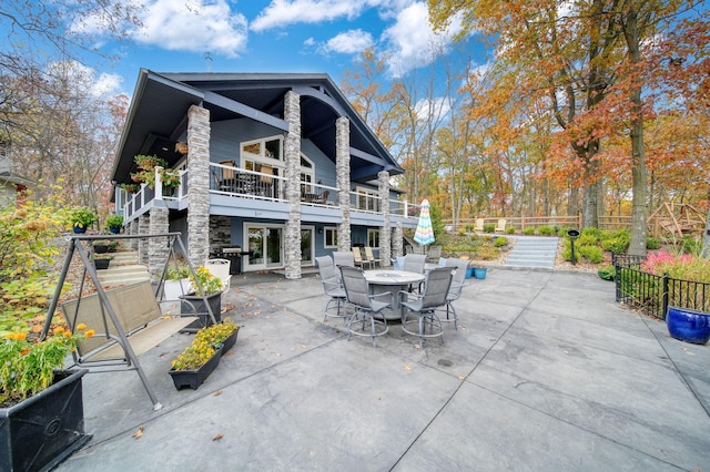 back of house with outdoor dining area, stone siding, a patio, and stairs