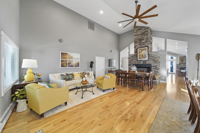 living room featuring a wealth of natural light, visible vents, wood finished floors, a stone fireplace, and baseboard heating