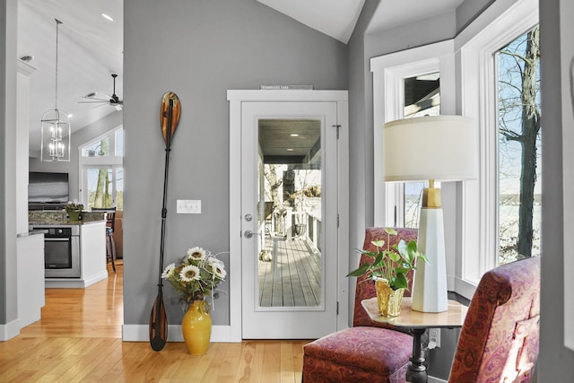 doorway to outside featuring vaulted ceiling, light wood-style flooring, and a notable chandelier