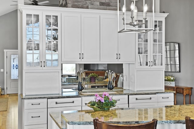 kitchen with light stone counters, glass insert cabinets, wood finished floors, and white cabinets