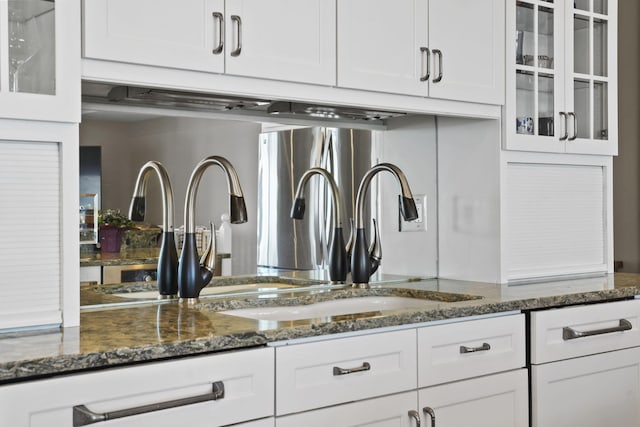 kitchen featuring white cabinets, dark stone counters, glass insert cabinets, and a sink