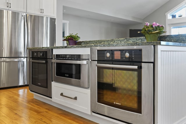 kitchen with light wood finished floors, white cabinetry, stainless steel appliances, and dark stone counters