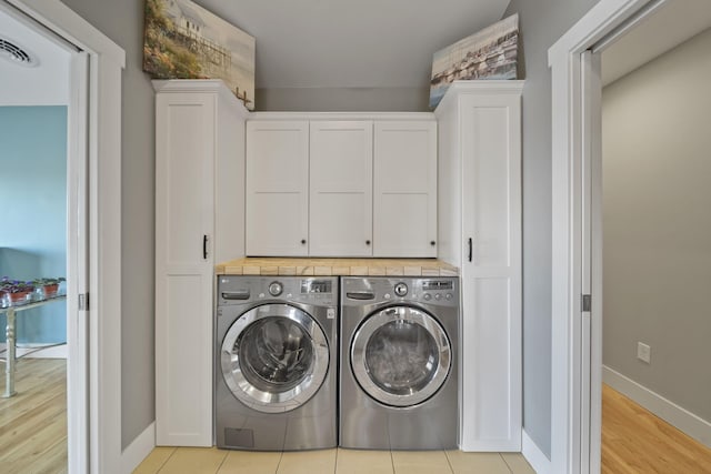 laundry area featuring visible vents, baseboards, washing machine and clothes dryer, cabinet space, and light wood-style floors