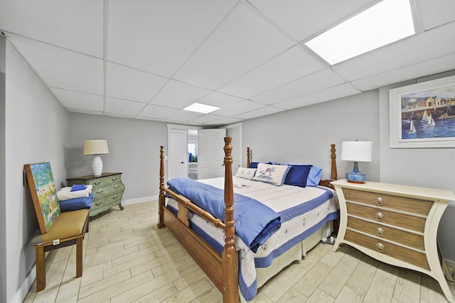 bedroom with a drop ceiling, baseboards, and light wood-style flooring