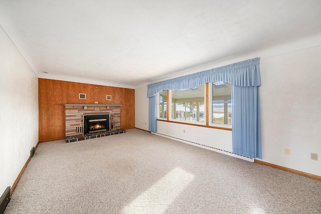 unfurnished living room featuring carpet flooring, wood walls, a stone fireplace, and baseboard heating