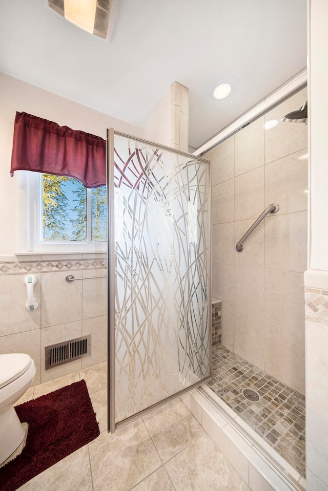 bathroom with tile patterned flooring, a tile shower, toilet, and tile walls