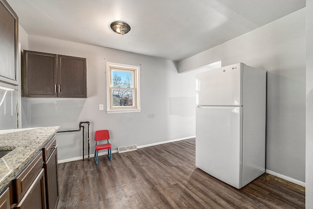 kitchen with light stone countertops, dark brown cabinets, white refrigerator, and dark wood-type flooring