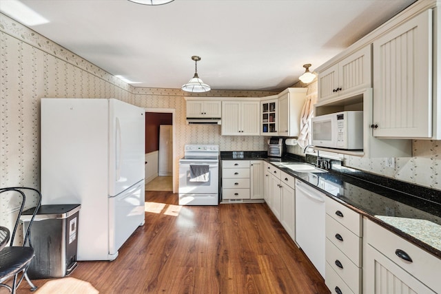 kitchen featuring sink, dark hardwood / wood-style flooring, dark stone countertops, pendant lighting, and white appliances