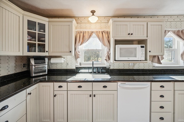 kitchen with a textured ceiling, white appliances, sink, and dark stone counters