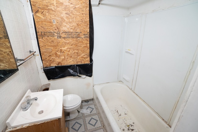 bathroom featuring a tub to relax in, vanity, tile walls, and toilet