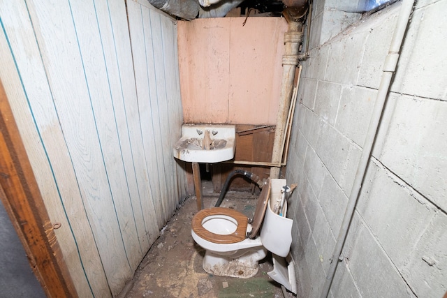 bathroom with wooden walls, concrete flooring, and toilet