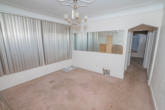 carpeted empty room featuring a textured ceiling and an inviting chandelier