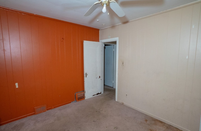 carpeted empty room with ceiling fan, crown molding, and wood walls