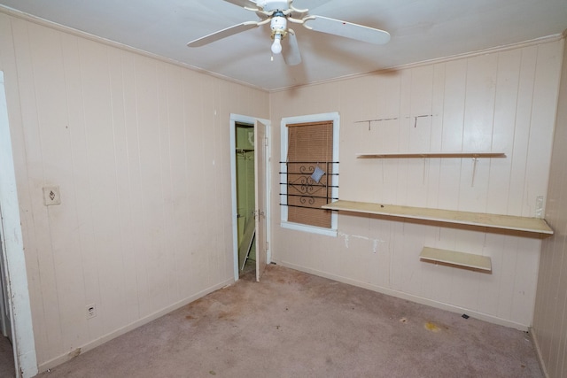 unfurnished room with light carpet, ceiling fan, crown molding, and wood walls