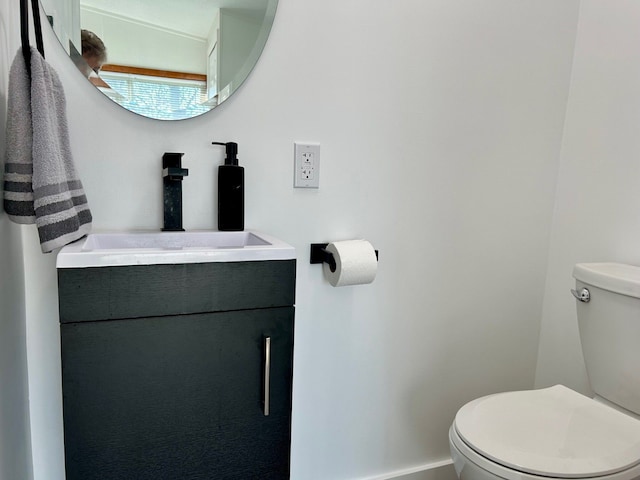 half bath featuring baseboards, vanity, and toilet