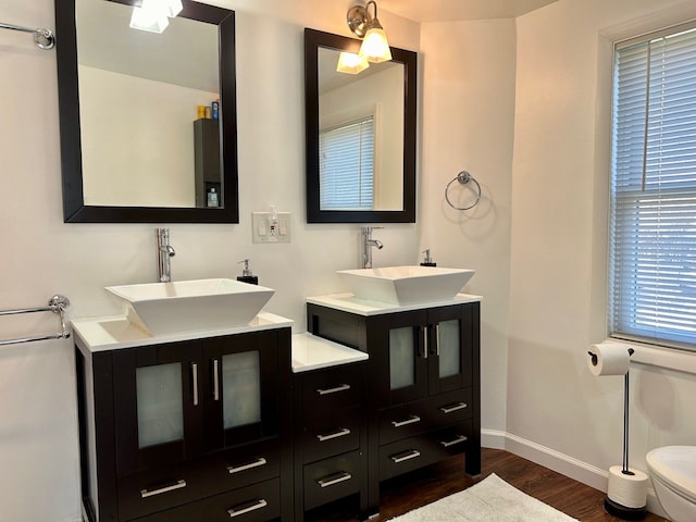 bathroom featuring wood finished floors, two vanities, a sink, and baseboards