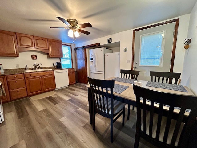 kitchen featuring white appliances, a barn door, light wood-style flooring, brown cabinets, and a sink