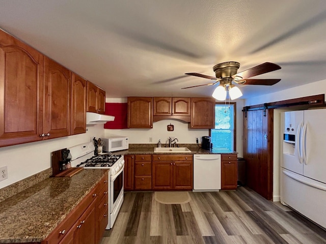 kitchen featuring white appliances, under cabinet range hood, dark wood-style flooring, and a sink