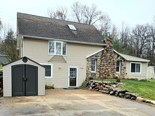 back of property featuring a storage shed, an outdoor structure, roof with shingles, a chimney, and a patio area