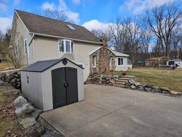 rear view of house featuring a lawn, a chimney, a storage unit, an outdoor structure, and a patio area