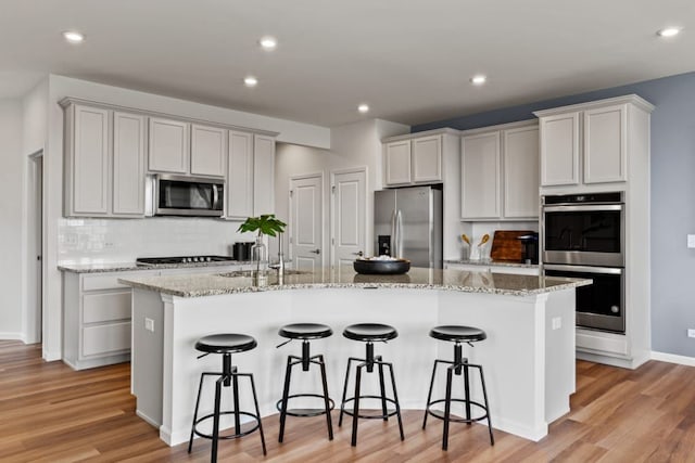 kitchen featuring white cabinetry, a kitchen breakfast bar, light wood-style floors, appliances with stainless steel finishes, and a center island with sink