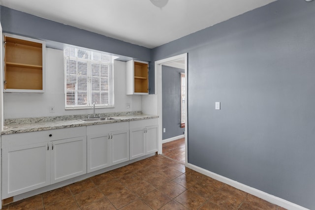 kitchen featuring light stone countertops, dark tile patterned flooring, white cabinetry, and sink