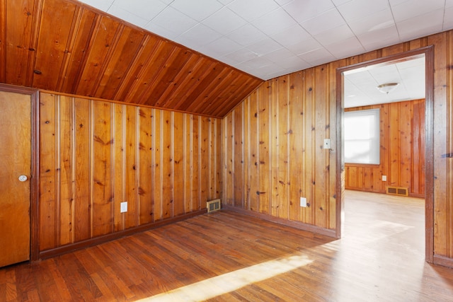 additional living space with wood walls, light hardwood / wood-style floors, and lofted ceiling