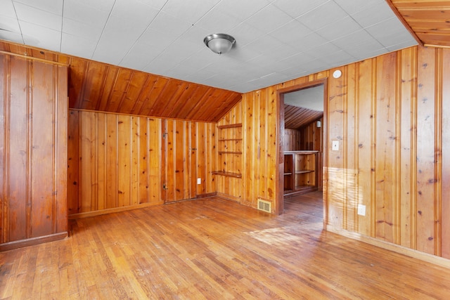 additional living space with wooden walls, hardwood / wood-style floors, and lofted ceiling