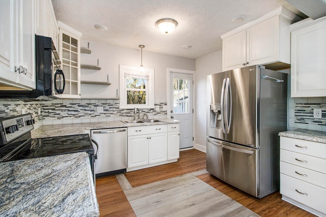 kitchen with sink, appliances with stainless steel finishes, decorative light fixtures, white cabinets, and light wood-type flooring