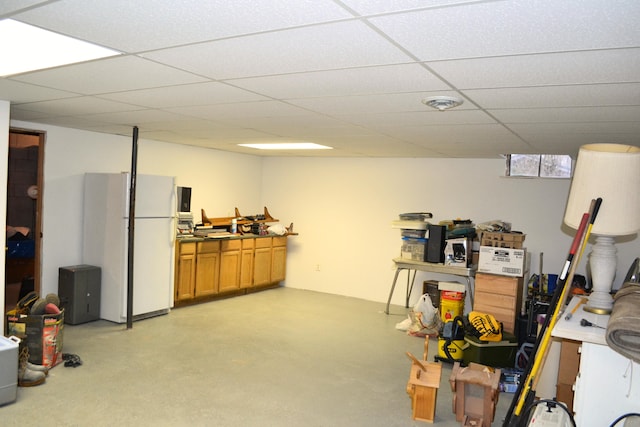 basement featuring a drop ceiling and white fridge