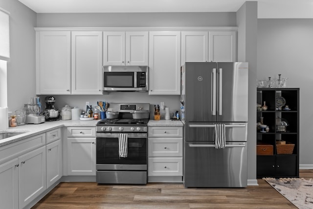 kitchen with white cabinets, sink, hardwood / wood-style flooring, light stone countertops, and stainless steel appliances