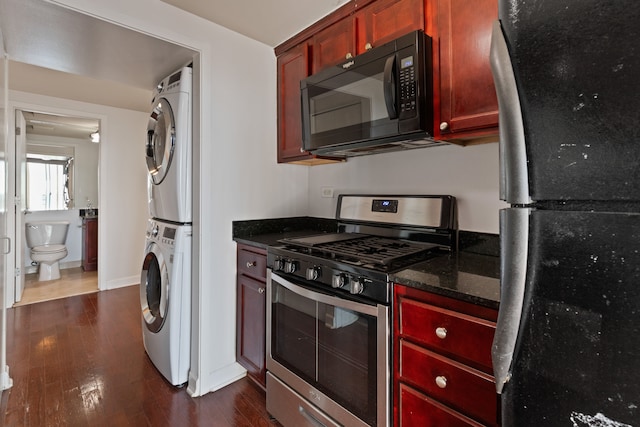 kitchen with dark stone counters, stacked washer / dryer, dark wood-type flooring, and black appliances