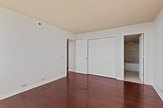 unfurnished bedroom with connected bathroom, a closet, dark wood-type flooring, and a textured ceiling