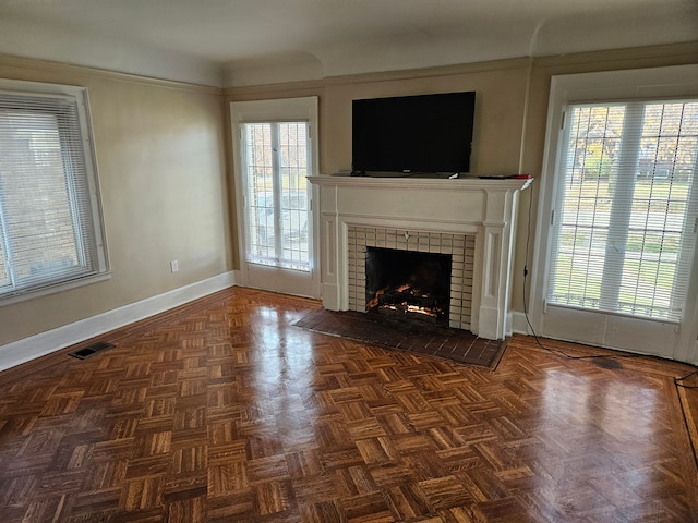 unfurnished living room featuring a fireplace, dark parquet flooring, and a healthy amount of sunlight