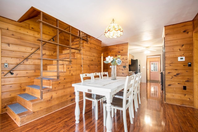 dining space with hardwood / wood-style floors, ceiling fan, and wooden walls