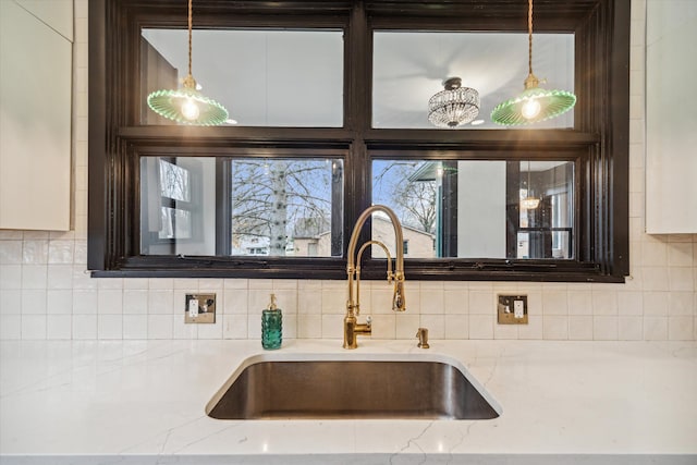 details with decorative backsplash, light stone counters, sink, and decorative light fixtures