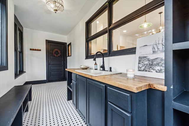 bar featuring butcher block countertops, sink, blue cabinetry, and hanging light fixtures